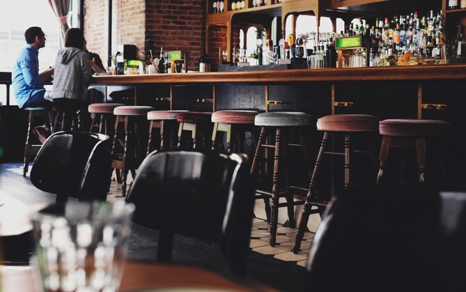 bar stools tucked in under bar, two people sitting at far end of bar.